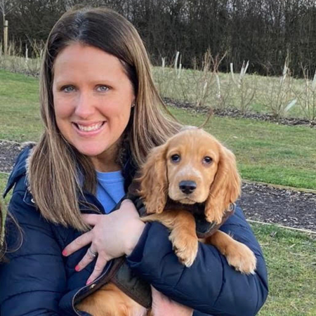 Dr Sarah Pilgrim is standing holding a puppy.